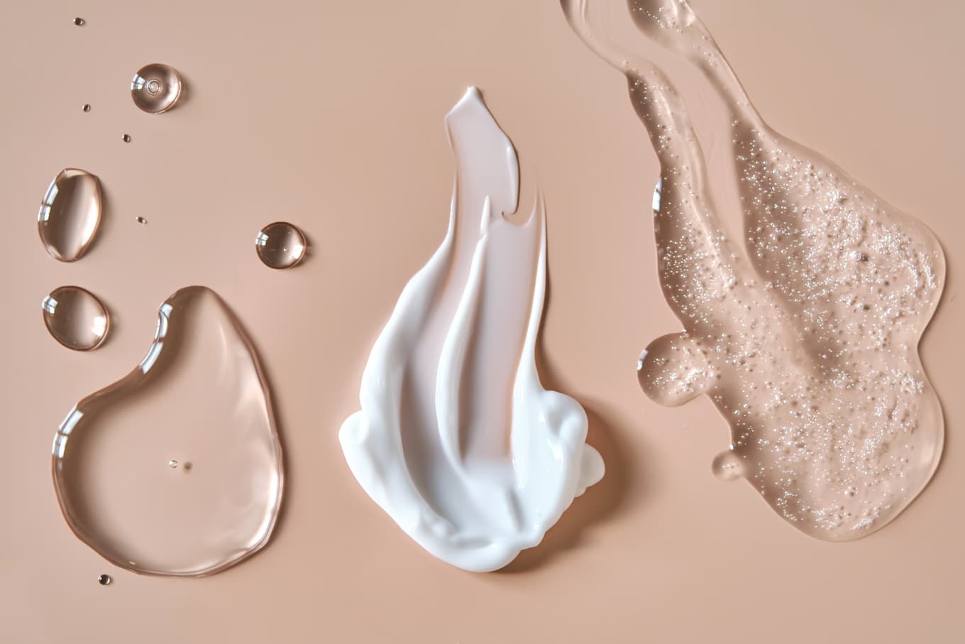 Verschiedene Hautpflege-Texturen wie Gel, Creme und Serum auf beigem Hintergrund