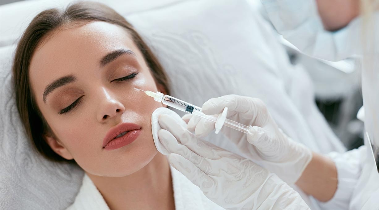 Frau bekommt Spritze mit Hyaluron gegen Falten ins Gesicht