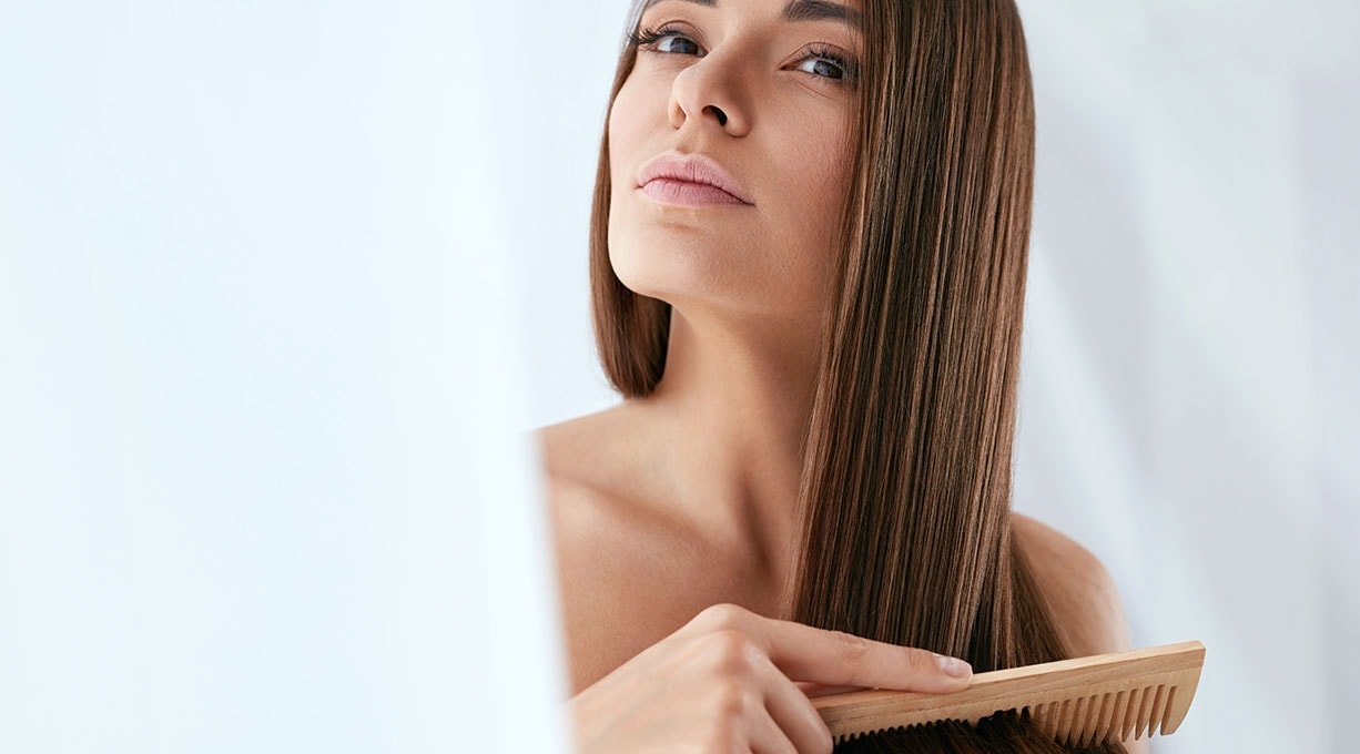 Frau mit glattem Haar kämmt ihre Haare, Sheabutter pflegt Haar und Kopfhaut