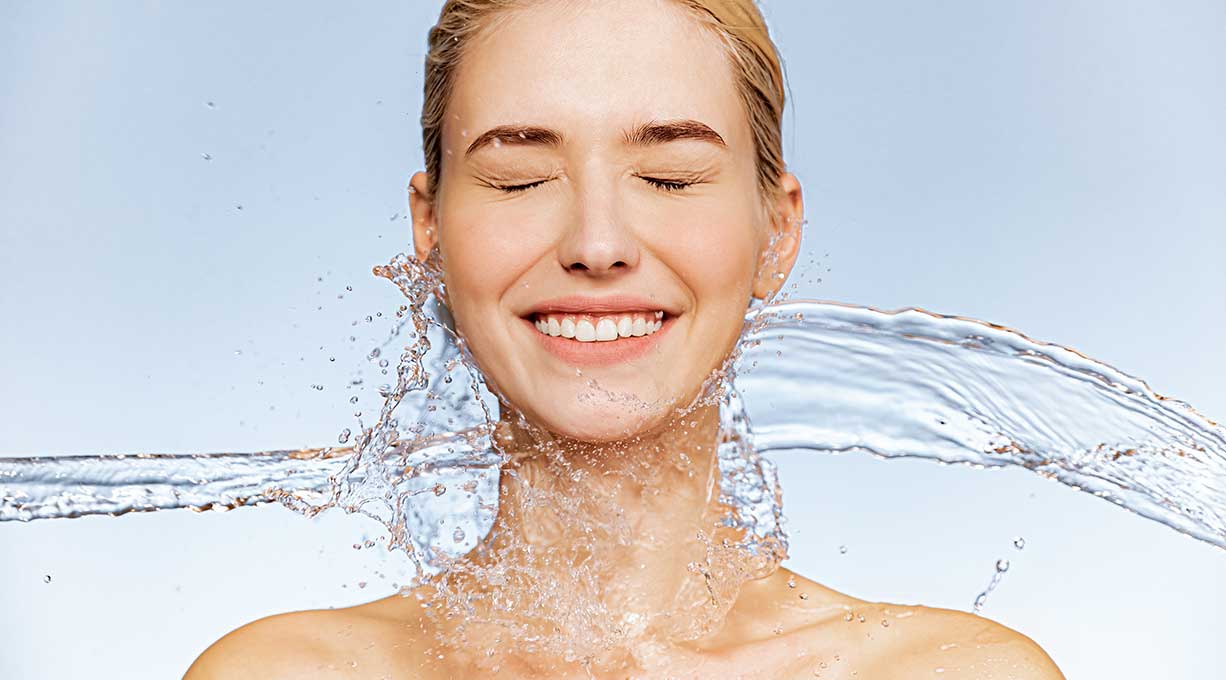 Lachende Frau wird von Wasser umspielt – steht für erfrischte, intensiv mit Feuchtigkeit versorgte Haut