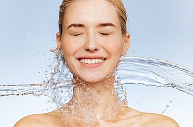 Lachende Frau wird von Wasser umspielt – steht für erfrischte, intensiv mit Feuchtigkeit versorgte Haut