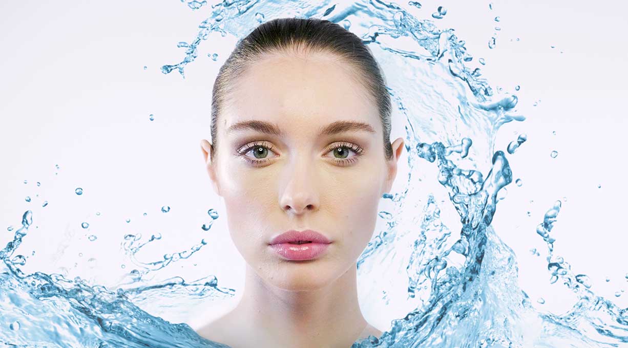 Frau mit frischer Haut, umgeben von Wasserspritzern – Symbol für intensive Feuchtigkeitspflege