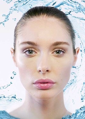 Frau mit frischer Haut, umgeben von Wasserspritzern – Symbol für intensive Feuchtigkeitspflege