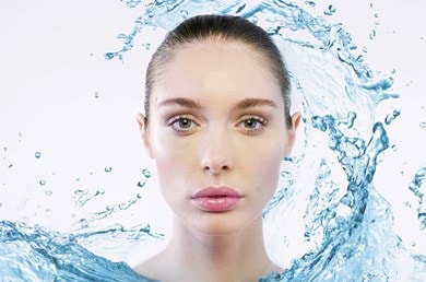 Frau mit frischer Haut, umgeben von Wasserspritzern – Symbol für intensive Feuchtigkeitspflege