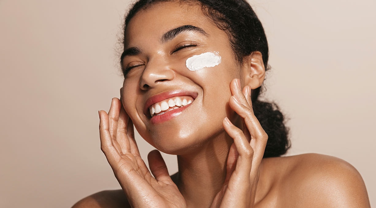 Lächelnde Frau mit Gesichtspflegecreme, strahlende Haut durch natürliche Feuchtigkeitsversorgung