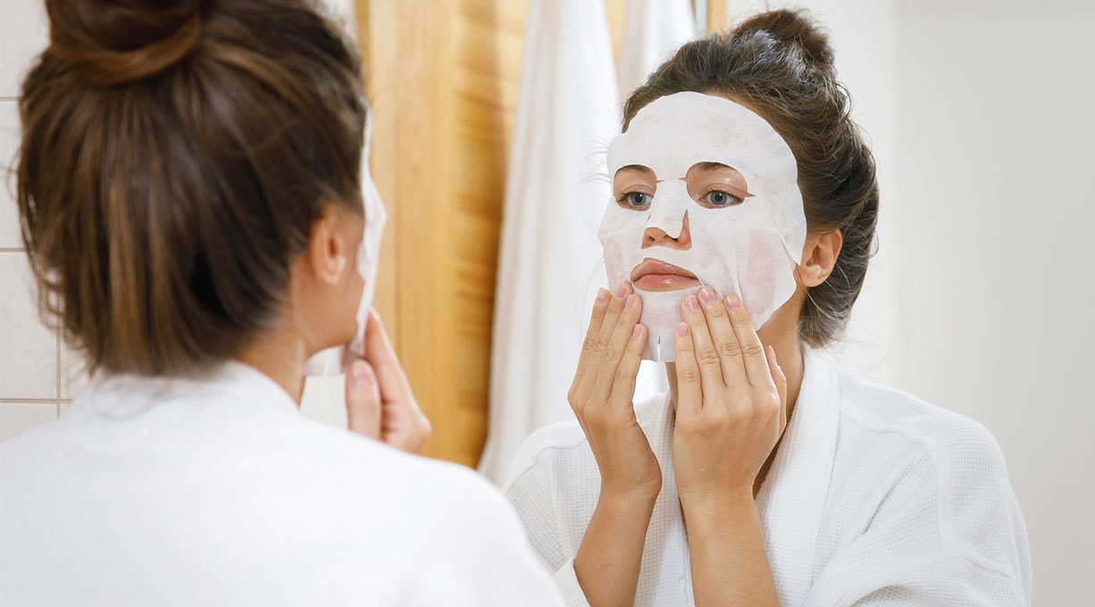 Frau trägt feuchtigkeitsspendende Tuchmaske auf, intensive Pflege für strahlend frische Haut