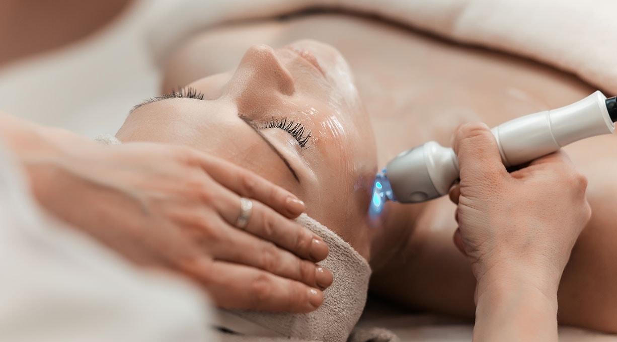 Eine liegende Frau lässt eine Gesichtsbehandlung beim Dermatologen machen