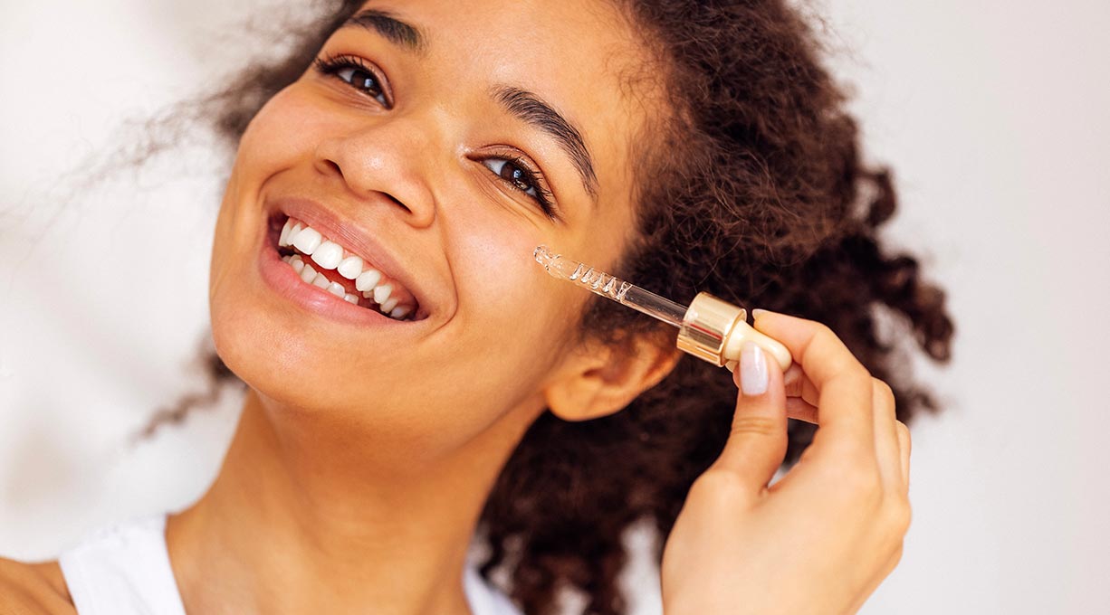 Lachende Frau trägt ein Serum mit Peptiden auf die Wange auf