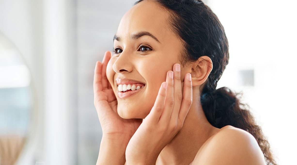 Lächelnde Frau hält sich ihre Hände an ihre Wangen