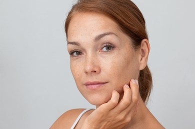 Frau mit Sommersprossen berührt leicht ihr Gesicht