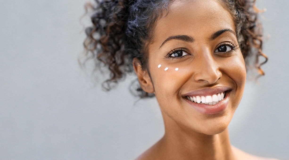 Lächelnde Frau mit drei Tropfen Augencreme unter ihrem rechten Auge