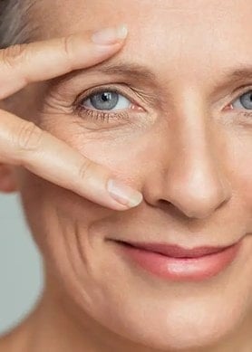 Ältere Frau lächelt und rahmt ihre Augenpartie mit ihrer Hand