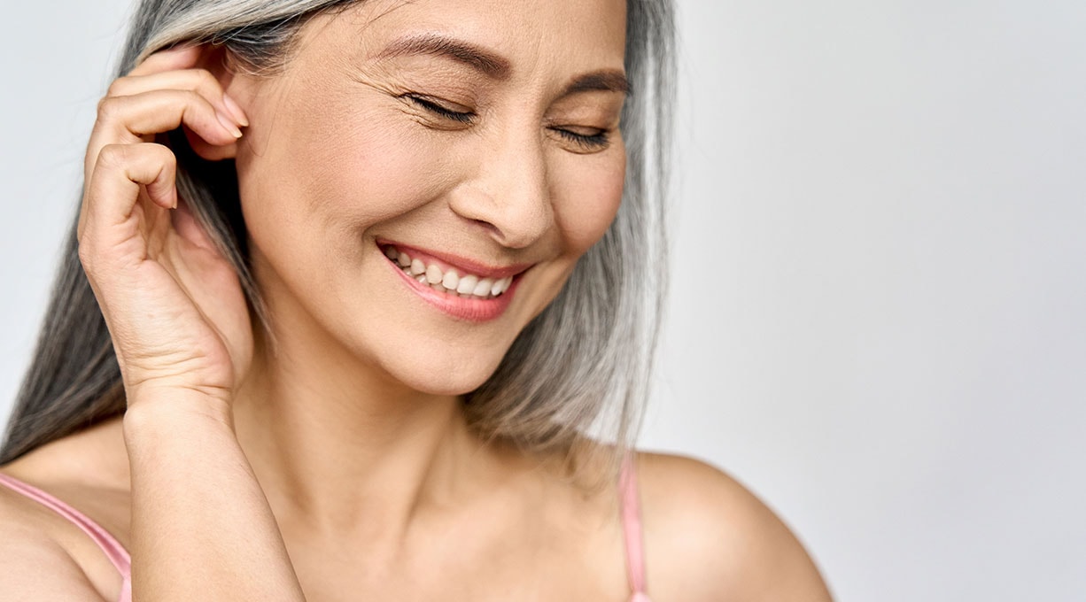 Ältere Frau mit grauen langen Haaren lächelt und schaut auf den Boden