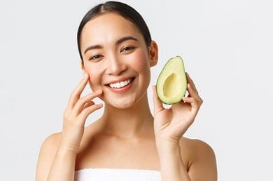 Eine Frau hält eine aufgeschnittene Avocado in die Kamera