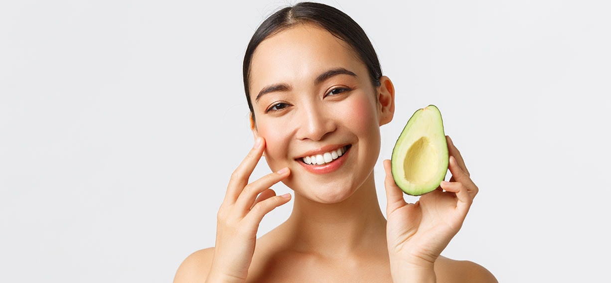 Eine Frau hält eine aufgeschnittene Avocado in die Kamera