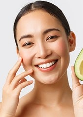 Eine Frau hält eine aufgeschnittene Avocado in die Kamera