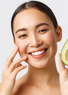 Eine Frau hält eine aufgeschnittene Avocado in die Kamera