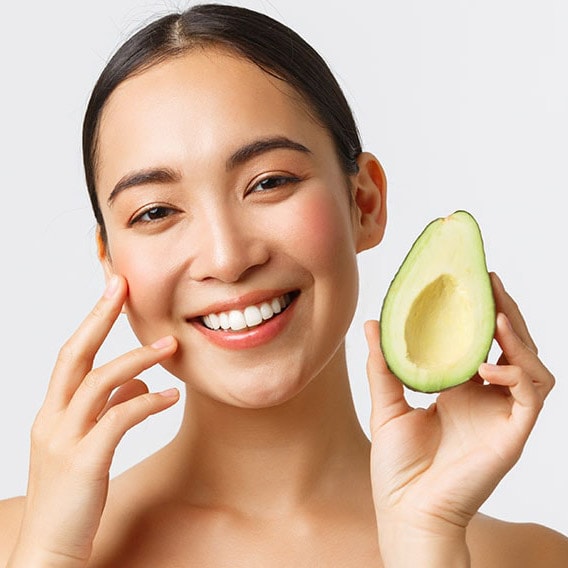 Eine Frau hält eine aufgeschnittene Avocado in die Kamera