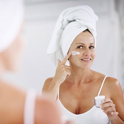 Frau mit Haarturban blickt in den Spiegel und cremt ihr Gesicht ein