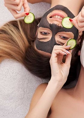 2 junge Frauen mit Gesichtsmasken und Gurkenscheiben in der Hand