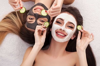 2 junge Frauen mit Gesichtsmasken und Gurkenscheiben in der Hand