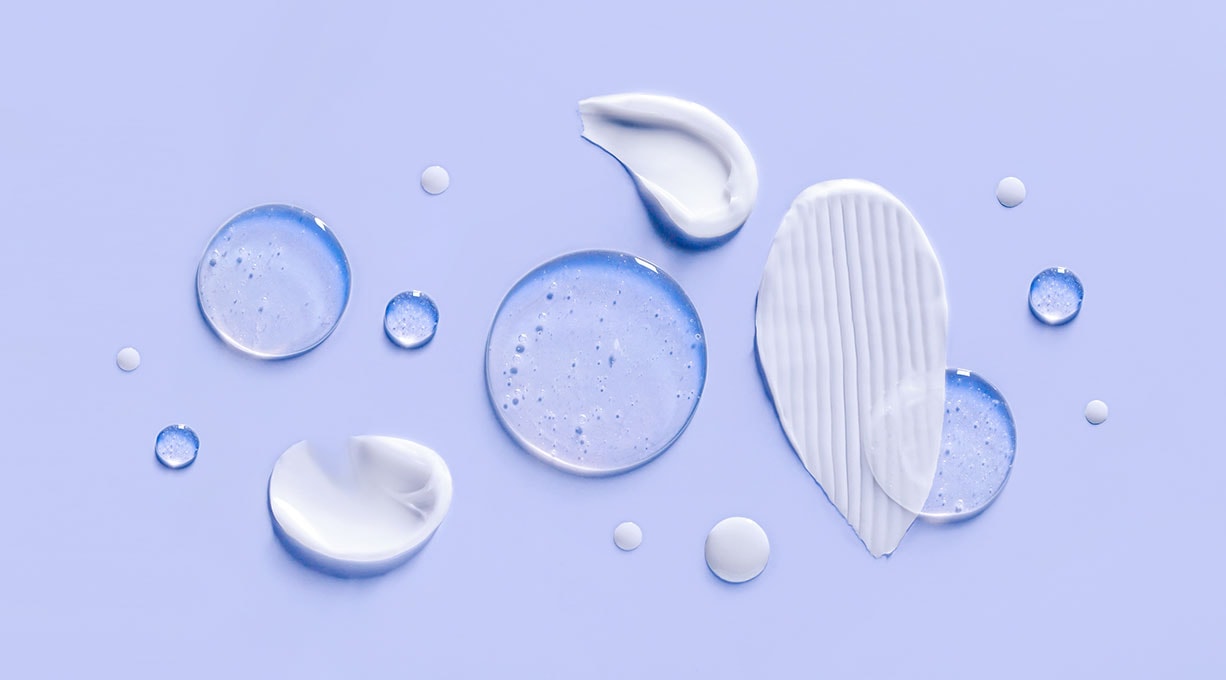 Wassertropfen und Cremeflecken auf einem lilafarbenen Untergrund