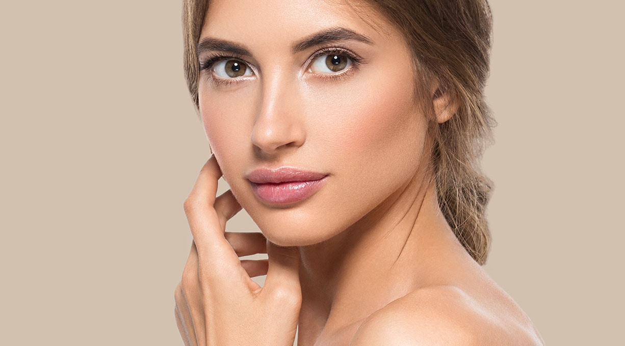 Eine junge Frau vor beigem Hintergrund sieht nach vorne