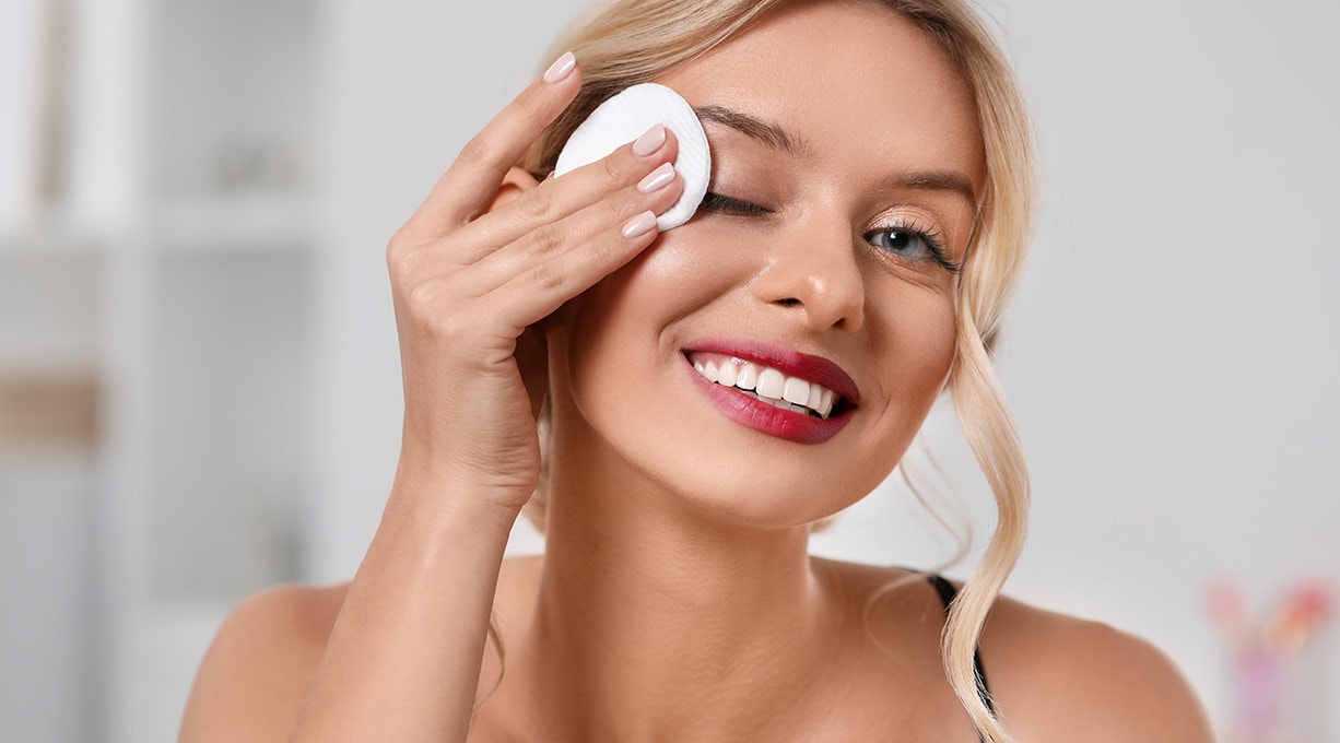 Blonde junge Frau schminkt sich mit einem Wattepad ab