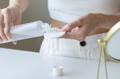 Person trägt Make-up-Entferner auf einem Wattepad auf