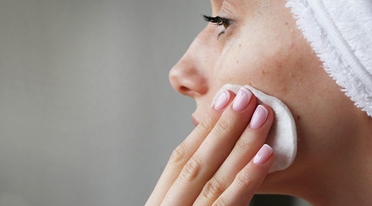 Eine Frau trägt Glykolsäure-Serum mit einem Wattepad auf ihre Haut auf