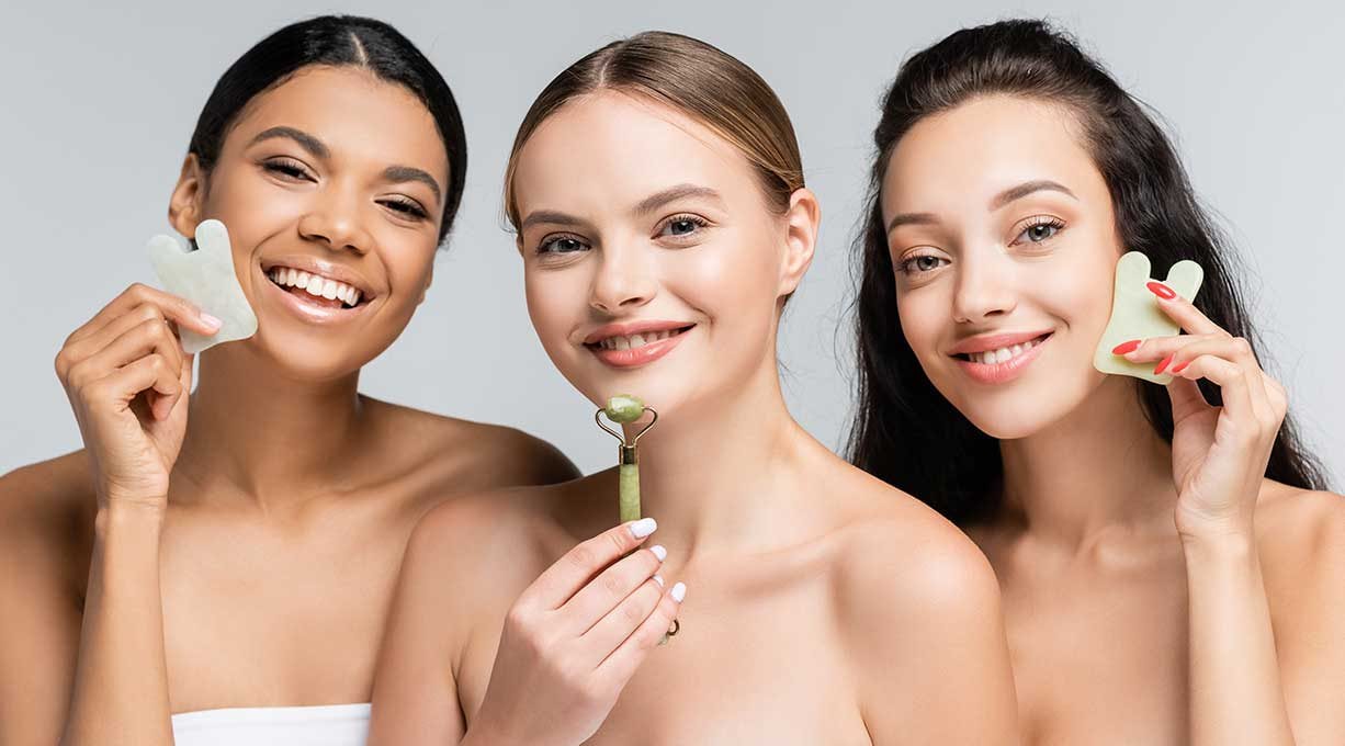 Drei junge Frauen halten verschiedene Gua Sha Tools für das Gesicht in der Hand