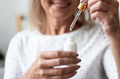 Ältere Frau lächelt während sie ein Gesichtsserum aus einer Pipettenflasche in der Hand hält