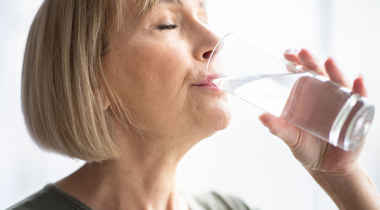 Eine ältere Frau mit kurzen blonden Haaren trinkt ein Glas Wasser