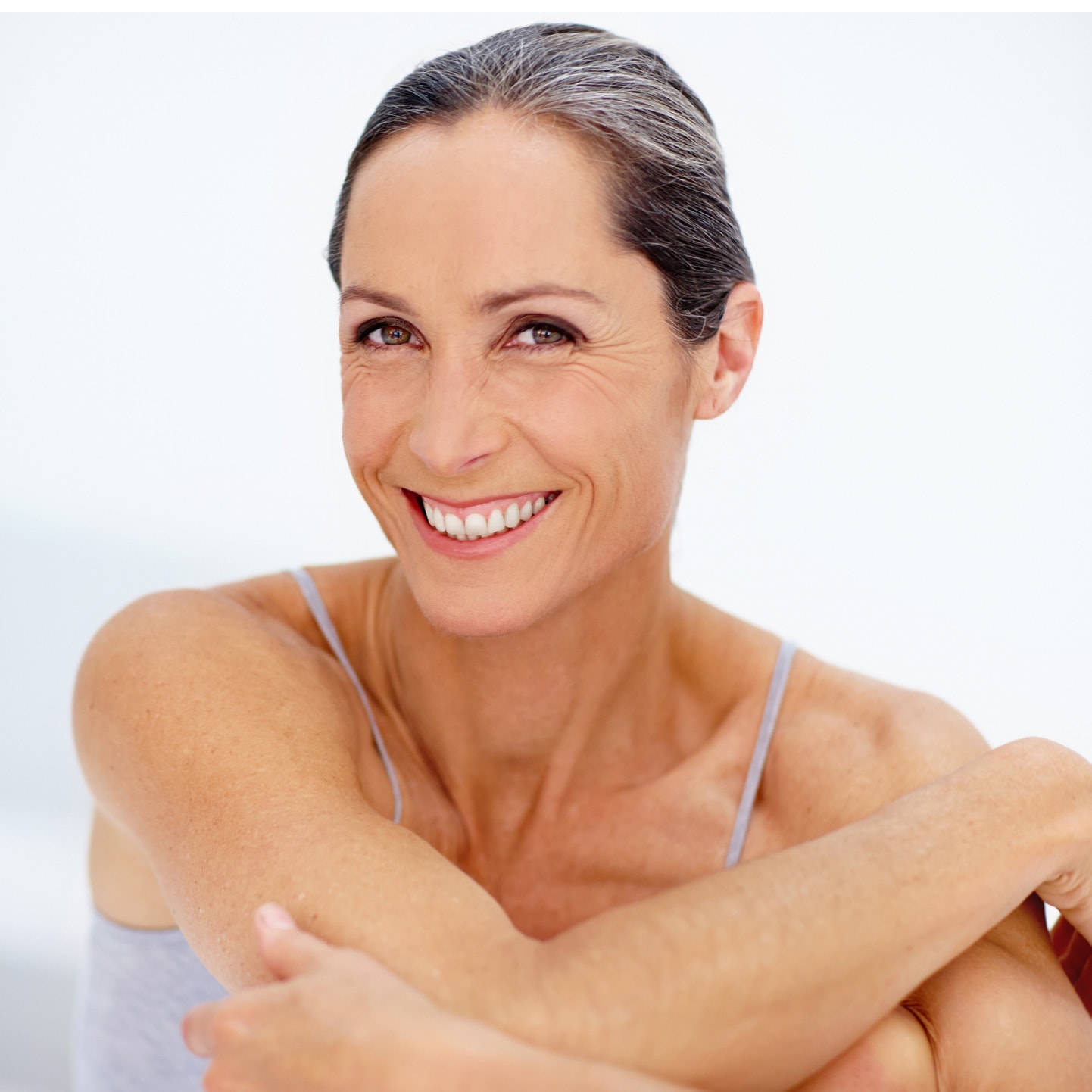 Lachende Frau mittleren Alters mit Mimikfalten und zurückgebundenen Haaren vor hellem Hintergrund