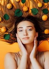 Frau liegt auf orangenem Untergrund, ihre langen Haare sind von Aprikosen bedeckt