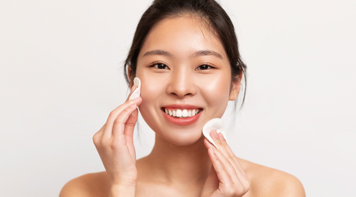 Junge Frau reinigt ihr Gesicht mit zwei Wattepads