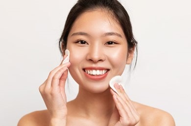 Junge Frau reinigt ihr Gesicht mit zwei Wattepads