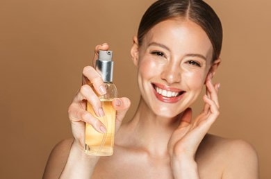 Junge Frau berührt lächelnd ihr Gesicht und hält ein Reinigungsöl in der Hand