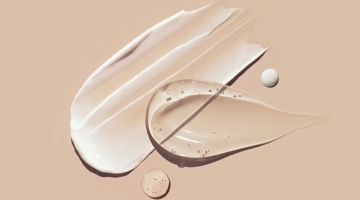 Etwas durchsichtiges Serum und etwas weiße Creme auf einem beigefarbenen Untergrund