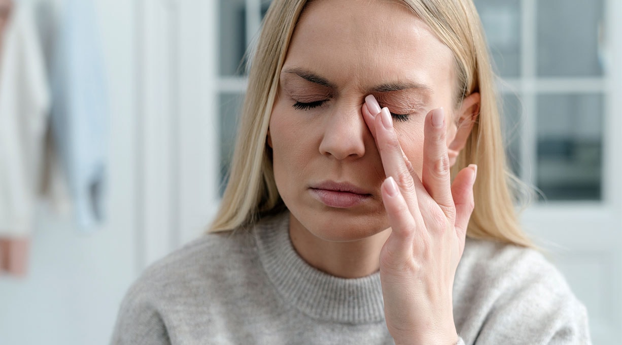 Frau mit geschlossenen Augen reibt sich ihr linkes Auge