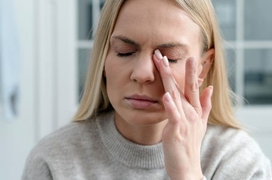 Frau mit geschlossenen Augen reibt sich ihr linkes Auge