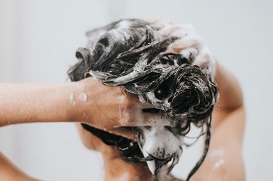 Eine Frau wäscht sich mit Shampoo unter der Dusche die Haare.