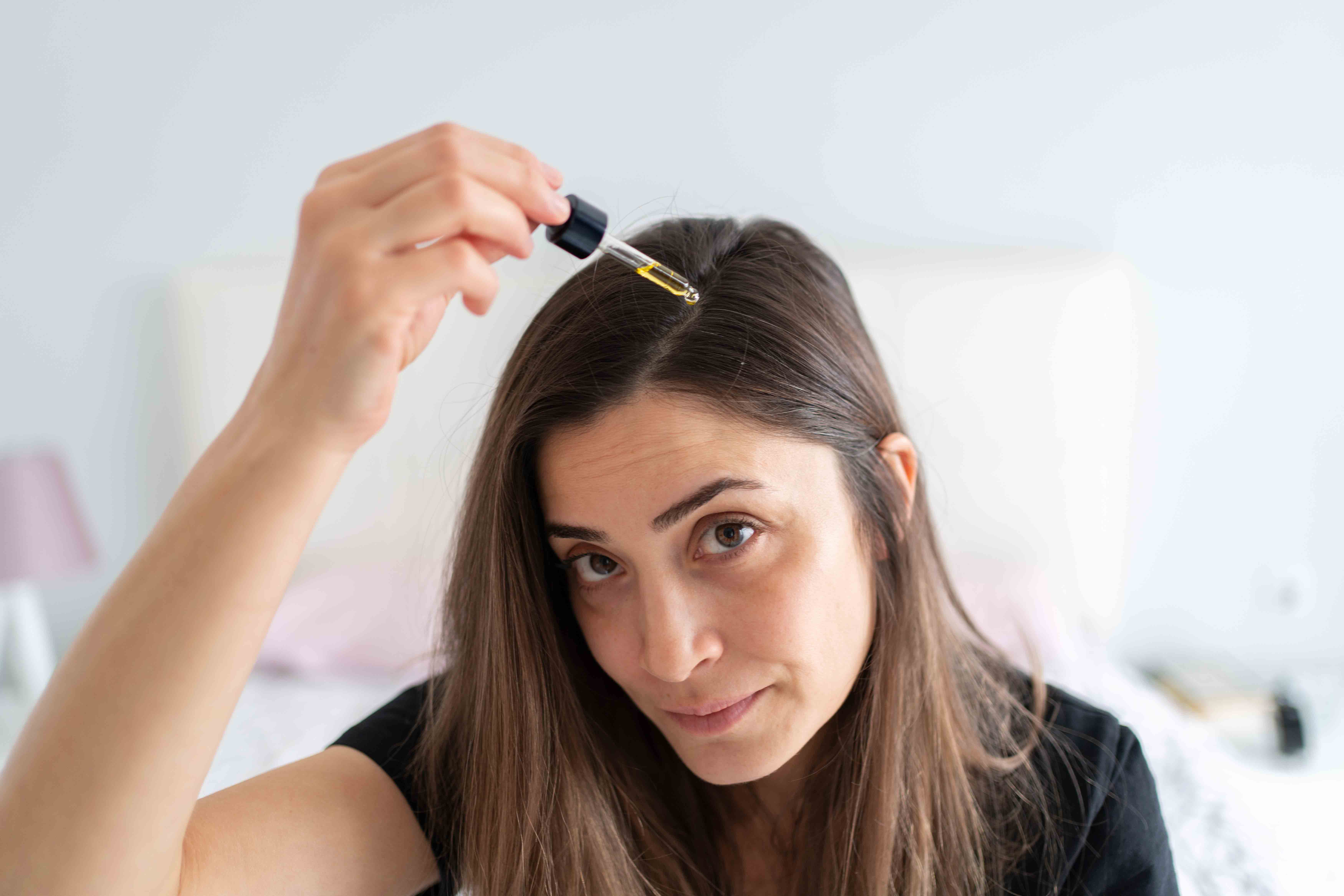 Frau trägt Serum mit Pipette direkt auf die Kopfhaut zur Pflege bei Haarausfall auf