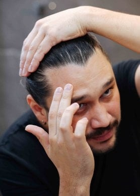 Mann betrachtet im Spiegel seinen Haaransatz und prüft möglichen Haarausfall im Badezimmer