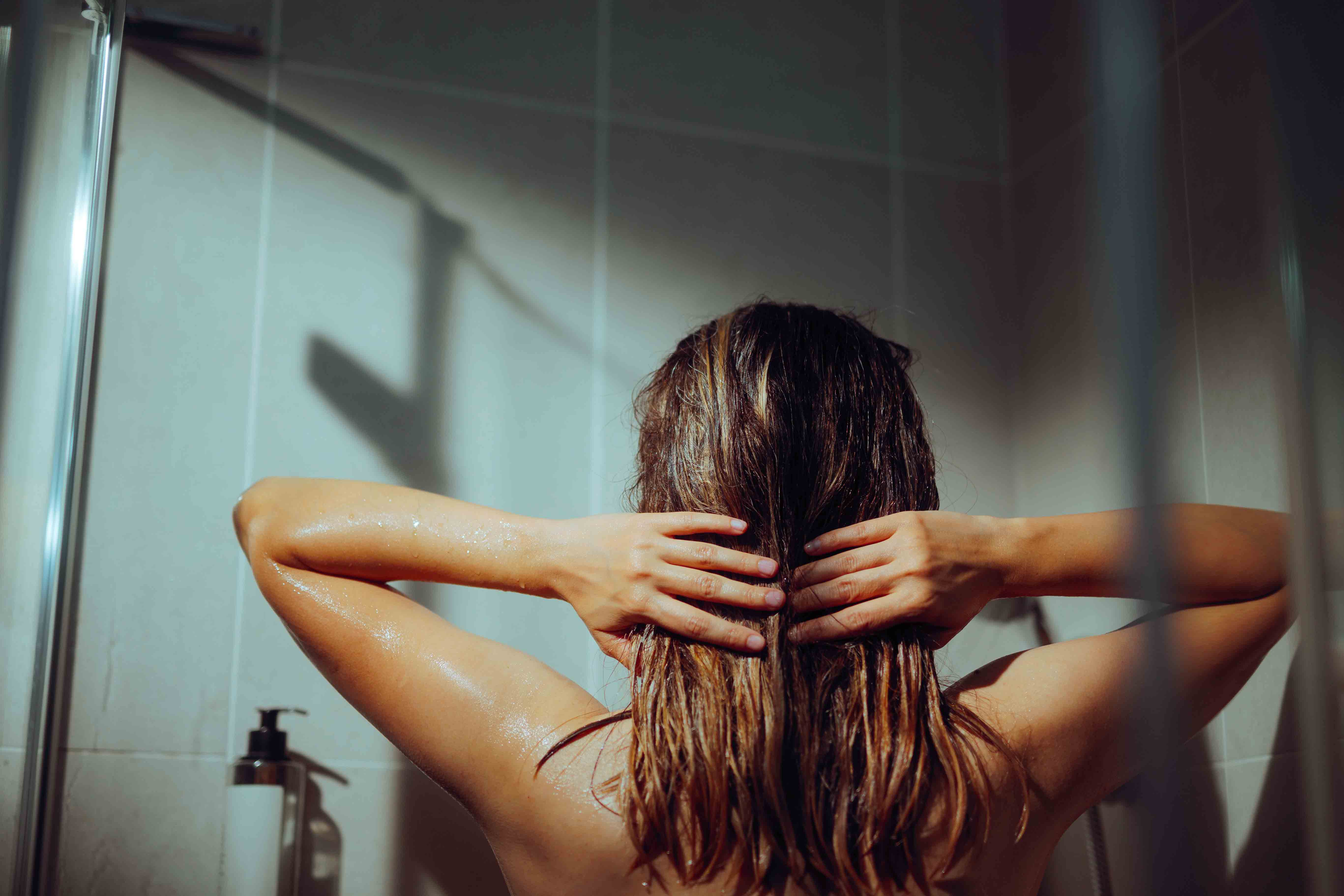 Frau massiert unter der Dusche Shampoo in nasses Haar ein