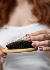 Frau betrachtet Haarausfall in der Haarbürste im Badezimmer
