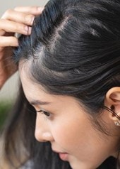 Eine Frau betrachtet ihren Haaransatz im Spiegel
