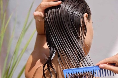 Frau mit braunen Haaren kämmt ihre nassen Haare mit einem grobzinkigen Kamm