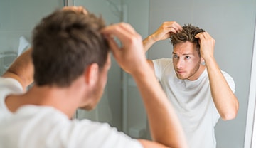 Mann überprüft seine Haare im Badezimmerspiegel und fährt mit den Händen durch das Haar