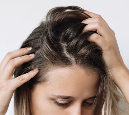 Frau streicht mit den Händen durch ihr Haar und inspiziert die Kopfhaut